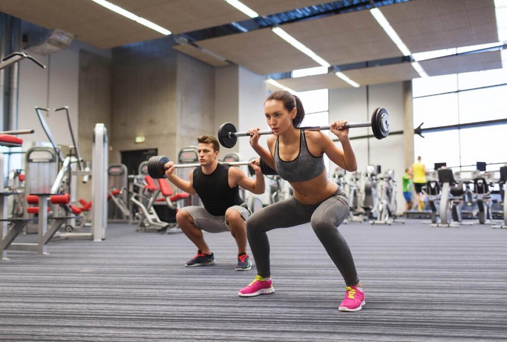 Male and female athletes performing barbell squats as part of strength training and physical therapy for athletes.