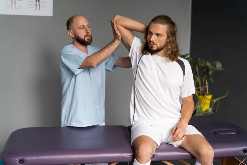 Physical therapist assisting male patient with shoulder mobility exercise during physical therapy for shoulder pain.