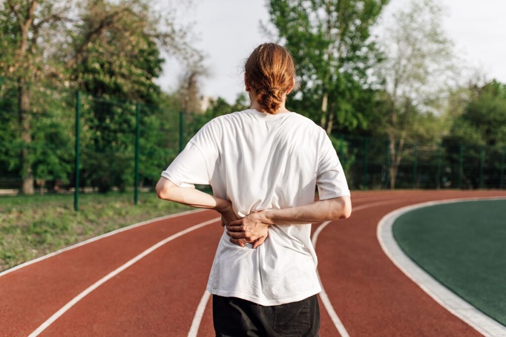 Runner holding hip in discomfort while on track, showing symptoms of hip pain from running.