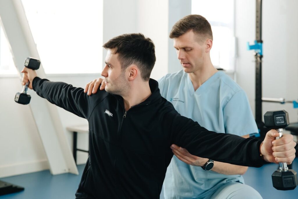 Physical therapist guiding a patient through a shoulder strengthening exercise with dumbbells, supporting recovery from a weightlifting rotator cuff injury and improving control through a safe range of motion.