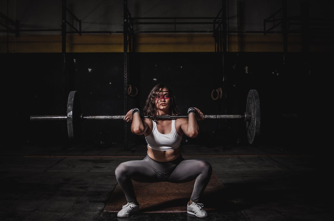 Athlete holding a barbell in the front rack position during a deep squat in a dark gym, illustrating a weightlifting rotator cuff injury risk during heavy shoulder loading.
