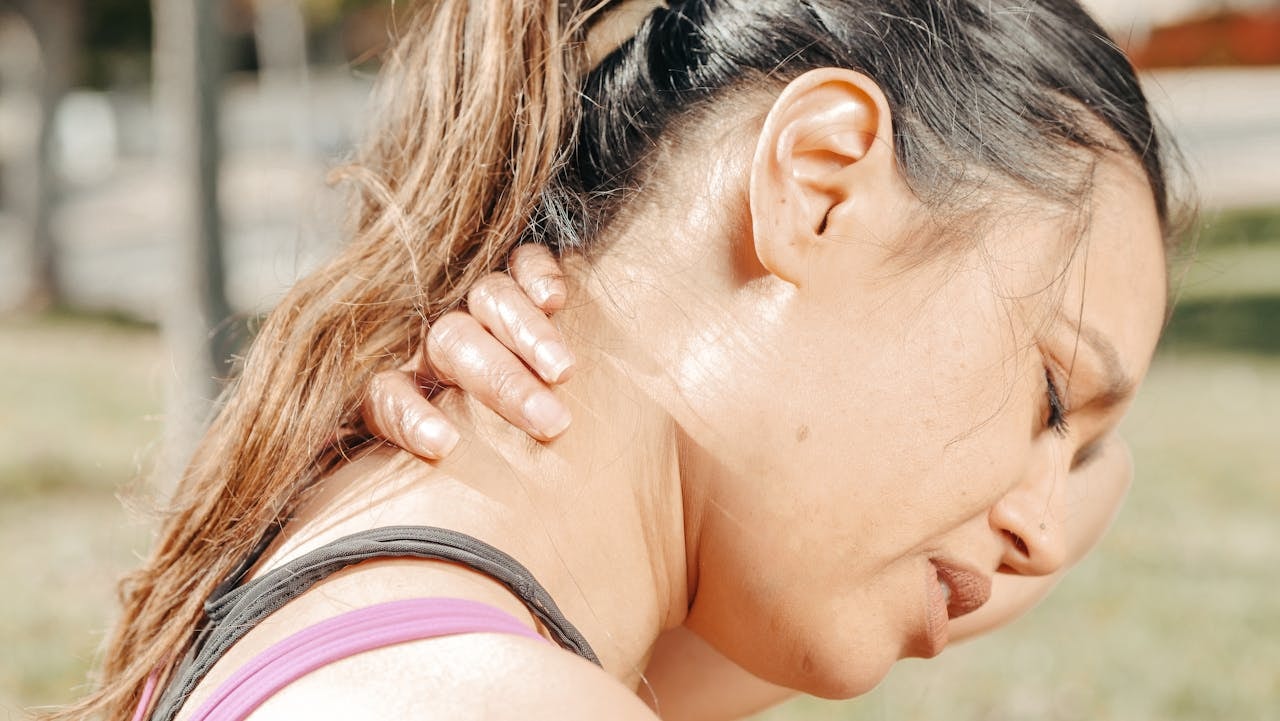 Woman outdoors rubbing the side of her neck with a pained expression, showing cervicalgia neck pain and neck stiffness.