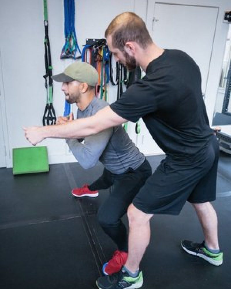 two men doing squats in a gym.