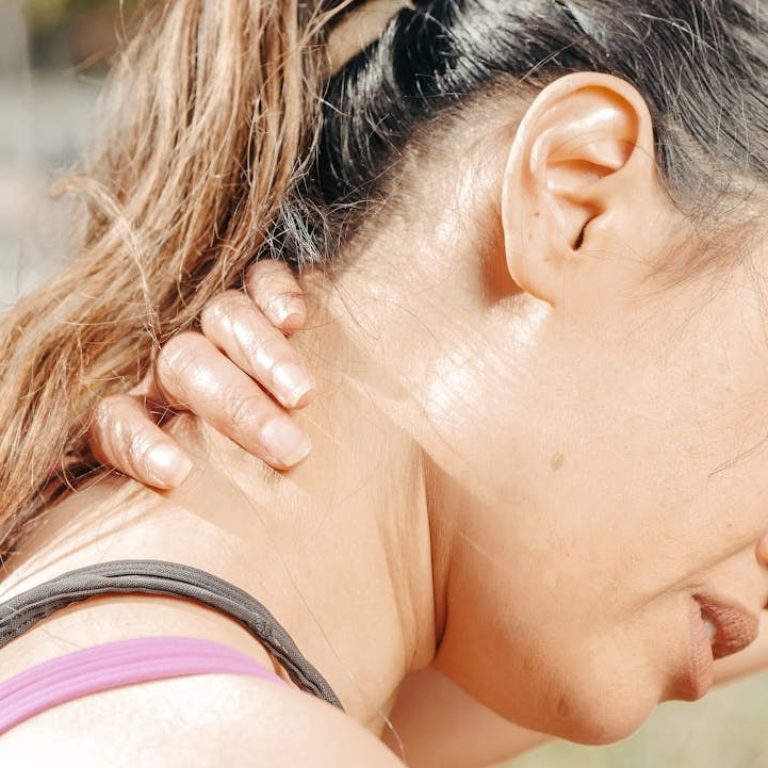 Woman outdoors rubbing the side of her neck with a pained expression, showing cervicalgia neck pain and neck stiffness.